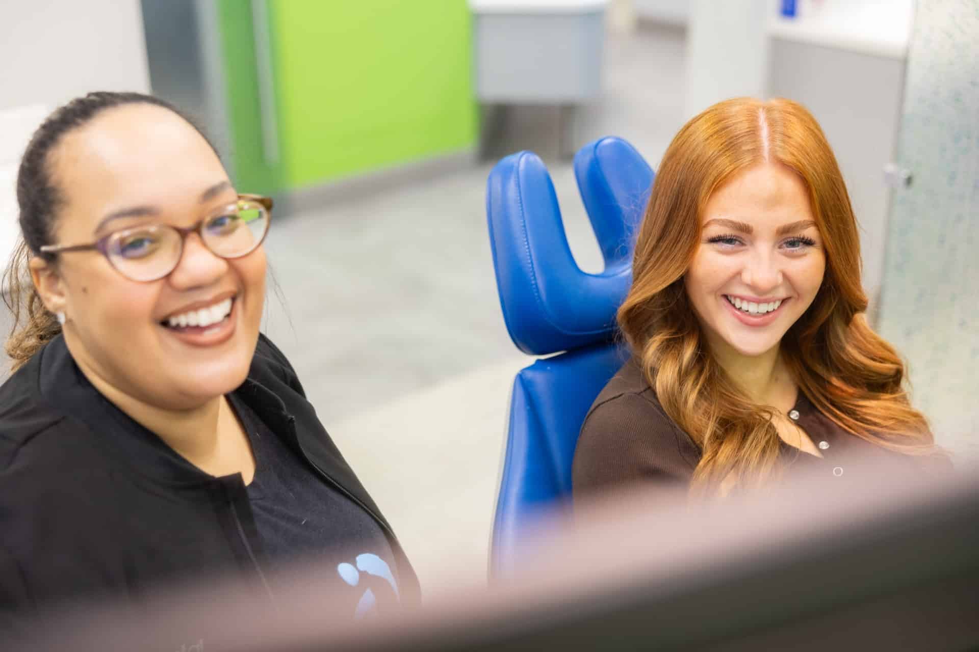 Two women smiling in dental clinic chair at Innovative Orthodontics — a team member and an adult orthodontic patient.